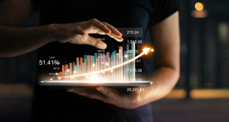 Person holding tablet with a hologram stock chart rising from the surface.