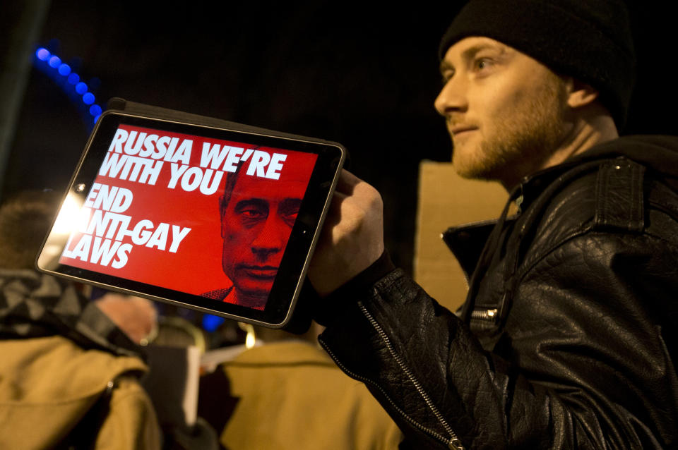 A Lesbian and Gay Rights activist holds up a tablet with a picture of a placard, during a demonstration aimed to coincide with the upcoming Winter Olympics in Sochi, Russia, against laws aimed at stifling Gay Rights in Russia, opposite Downing Street in London, Wednesday, Feb. 5, 2014. In London, about 150 people rallying outside Prime Minister David Cameron's office in London urged McDonald's and the IOC's other sponsors to speak out. The activists there said they plan to deliver a petition signed by more than 100,000 people to a nearby McDonald's restaurant. (AP Photo/Alastair Grant)