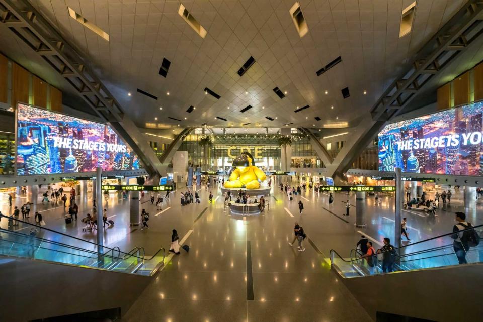 Many tourists are in the Hamad International Airport Terminal with Big Yellow Bear Sculpture