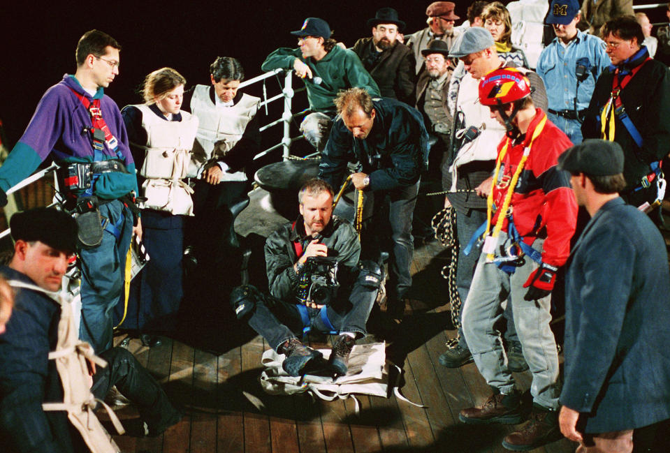 Cameron holding a camera surrounded by many crew members on the set 