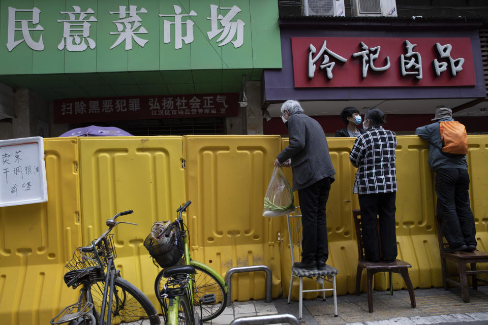 FILE - In this April 3, 2020, file photo, residents climb onto chairs to buy groceries from vendors behind barriers used to seal off a neighborhood in Wuhan in central China's Hubei province. The Chinese city of Wuhan is looking back on a year since it was placed under a 76-day lockdown beginning Jan. 23, 2020. (AP Photo/Ng Han Guan, File)
