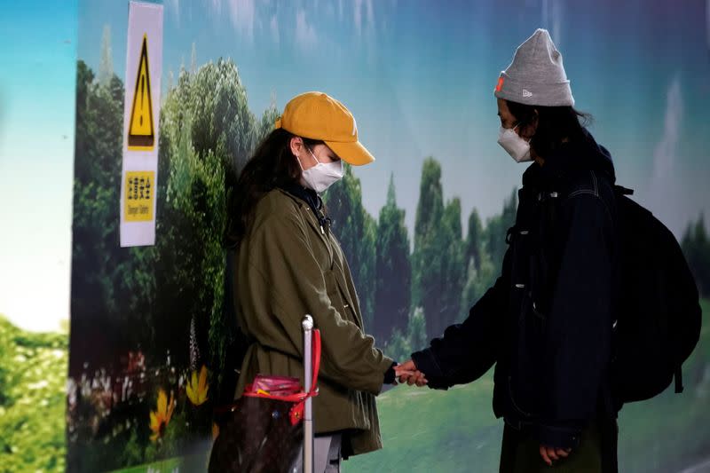A couple wearing masks holds hands at Pudong International Airport in Shanghai
