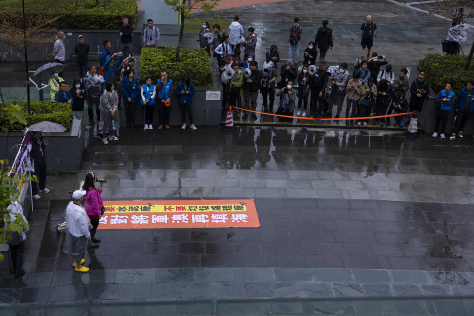 Protesters, left, stage a rally as member of the press, right, stand in a cordoned area in Hong Kong, Sunday, March 26, 2023. Dozens of people on Sunday joined Hong Kong's first authorized demonstration against the government since the lifting of major COVID-19 restrictions under unprecedentedly strict rules, including wearing a numbered badge around their necks. (AP Photo/Louise Delmotte)