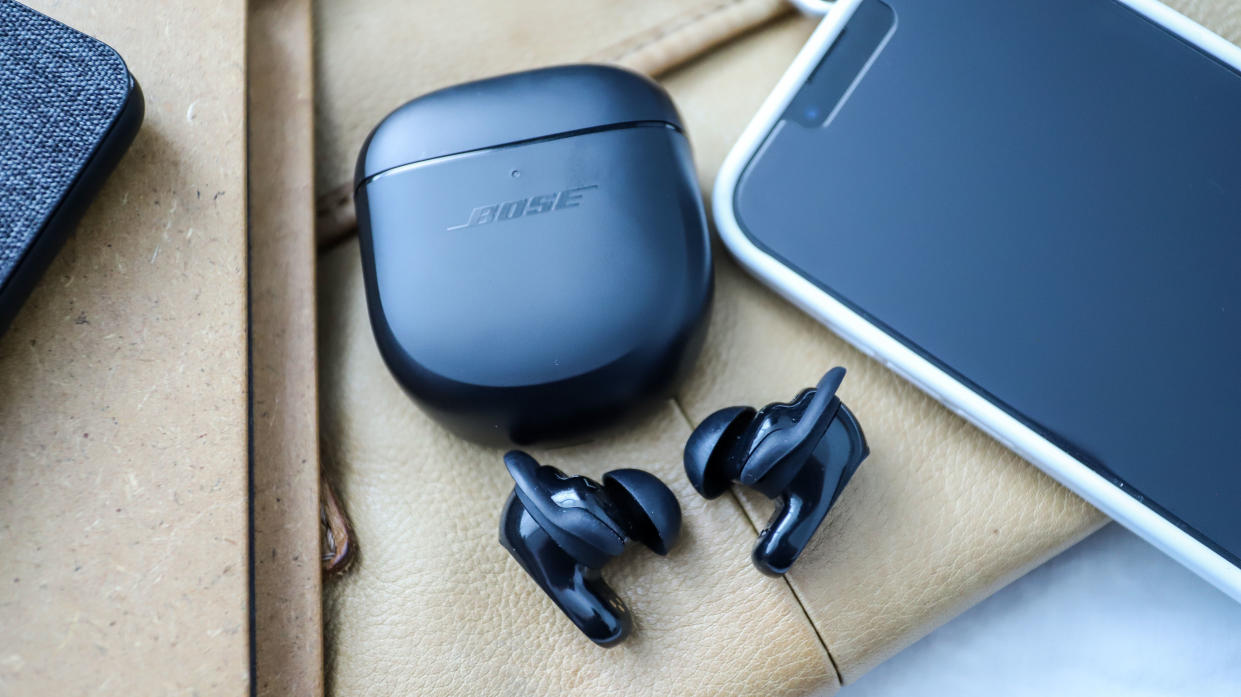  Bose QuietComfort Earbuds 2 lying beside their case and a phone 