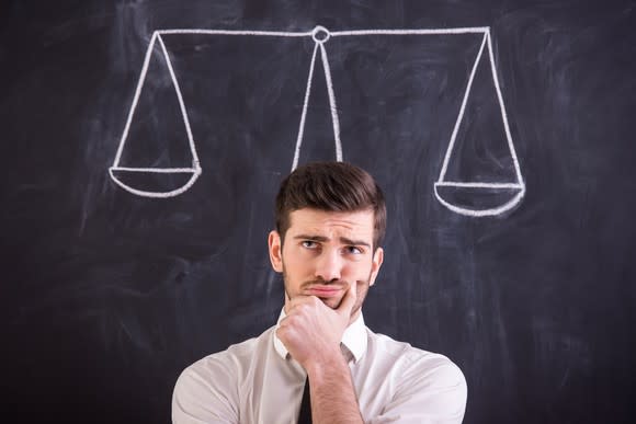 Man with hand on chin thinking in front of chalkboard with scales drawn on it