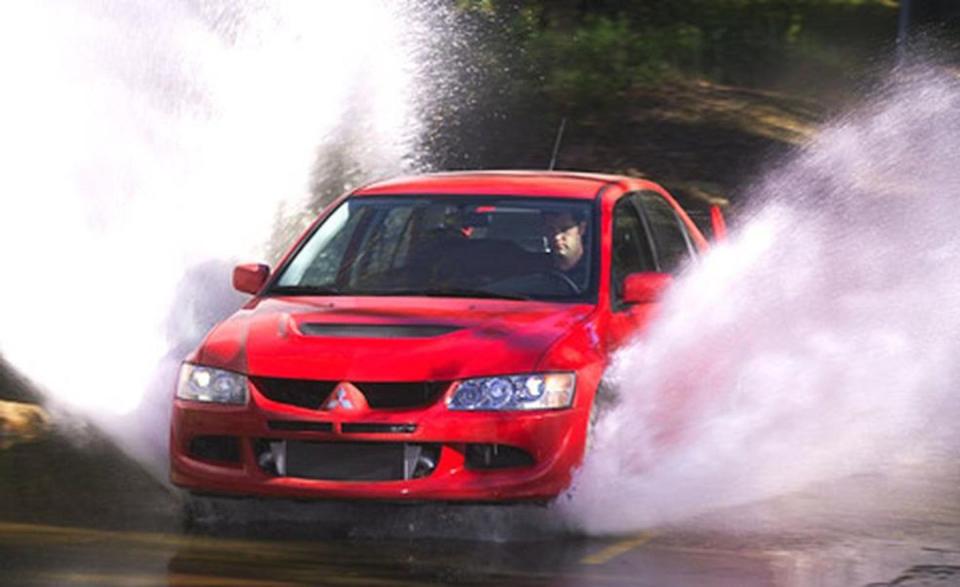 By 2003, Mitsubishi was finally ready to bring the Lancer Evolution to America. “Mitsubishi introduced the Evolution to this country at the Los Angeles auto show last January,” wrote a prepubescent Dan Pund in a <a href="http://www.caranddriver.com/comparisons/2003-mitsubishi-lancer-evolution-vs-subaru-impreza-wrx-sti-comparison-tests" rel="nofollow noopener" target="_blank" data-ylk="slk:June 2003 comparison test of the Evo VIII and the Subaru WRX STi;elm:context_link;itc:0;sec:content-canvas" class="link ">June 2003 comparison test of the Evo VIII and the Subaru WRX STi</a>. “The company basked in the adoring glow of the Evo's 44-hp advantage over the WRX—for all of one week. Then Subaru dropped its surprise 300-hp bomb on the awestruck at the Detroit show—days later in January—in the form of the STi model (for the company's in-house tuner, Subaru Tecnica International). One Mitsubishi official was seen seizing his crotch in mock pain over the blow dealt by Subaru.”<br><br>The still 271-horsepower Evo VIII defeated the WRX STi in that comparison test, and it impressed in almost every way. "Its transverse-mounted 2.0-liter DOHC in-line four is turbocharged to within an inch of its life with a maximum of 19.5 pounds of boost,” Pund explained. “Consequently, its power delivery is, at best, uneven. At low speed, there's a two-second gap between throttle application and full turbo boost. Then the engine virtually explodes with power, the turbo hissing in sinister fashion.” Praise came for its brilliant steering, “telepathic handling,” and huge rear wing that was “actually kind of cool.”<br><br>While criticizing some elements of the chintzy interior, the front Recaro seats were well appreciated. “As with virtually every other aspect of the car, Mitsubishi spent its money where it counts most, on the driving experience.”