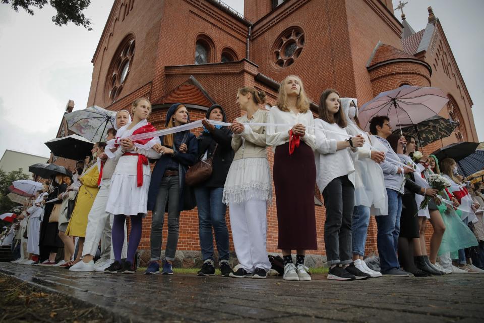 FILE - Protesters hold a ribbon in a symbol of protest in front of the Sts. Simon and Helena Catholic Church during a protest in Minsk, Belarus, on Thursday, Aug. 27, 2020. About 100 people took refuge from police in the landmark known as the “Red Church” for the color of its bricks. Authorities later said the church could not hold services. (AP Photo, File)