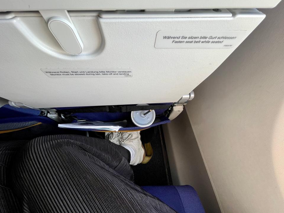 A view from above a pair of feet resting in a foot hammock under an airplane seat.