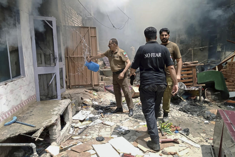 In this photo provided by the district police office, a police officer pours water into a burning house in a Christian neighborhood following an angry mob attack in Jaranwala near Faisalabad, Pakistan, Wednesday, Aug. 16, 2023. A Muslim mob stormed a Christian locality in Pakistan's eastern Punjab province, burning three churches and demolishing the house of a man after accusing him of desecrating the pages of Islam's holy book, police said. (District Police Office via AP)