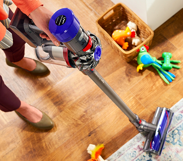 Woman using Dyson V8 Animal Pro on rug and hardwood.