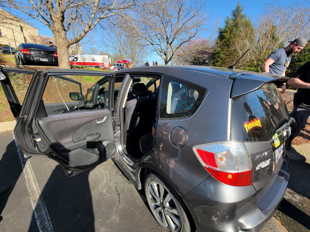 The Honda Fit vehicle with its two left doors open, beside a grassy area with trees, with the school in the background.