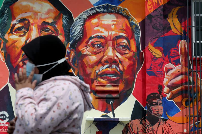FILE PHOTO: A woman passes by a mural depicting Malaysia's Prime Minister Muhyiddin Yassin in Kuala Lumpur