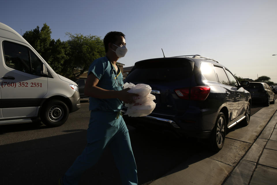 Dr. Tien Vo carries food for a family quarantining after testing positive for the coronavirus Thursday, July 23, 2020, in Calexico, Calif. Vo moved to Imperial Valley ten years ago. He says he stayed because people are friendly and appreciative. He sees happiness in their eyes when they greet him. "They really need a doctor here," he says from the front seat of a company van between house calls. "They're not very hard to please. They chat with me. They text me every day." (AP Photo/Gregory Bull)