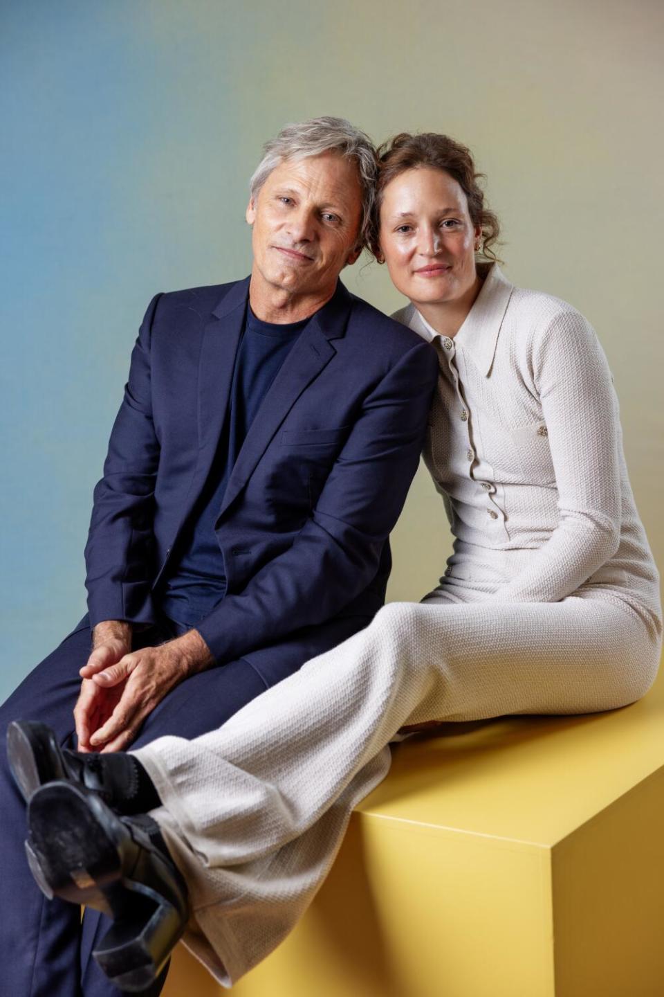 Viggo Mortensen and Vicky Krieps lean into each other while sitting on a cube.