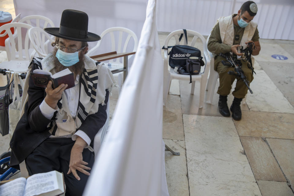 With a social distancing barrier, an ultra-Orthodox Jewish man and an Israeli soldier pray ahead of Yom Kippur, the holiest day in the Jewish year which starts at sundown Sunday during a three-week nationwide lockdown to curb the spread of the coronavirus at the Western Wall, in Jerusalem's old city, Sunday, Sept. 27, 2020. (AP Photo/Ariel Schalit)