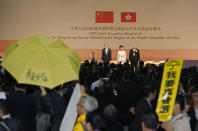 FILE - A protester raises an umbrella and placard reading: "I want genuine universal suffrage" to protest as former Hong Kong Chief Secretary Carrie Lam, center, declares her victory in the chief executive election of Hong Kong while former Financial Secretary John Tsang, left, and retired judge Woo Kwok-hing stand with her in Hong Kong on March 26, 2017. (AP Photo/Kin Cheung, File)