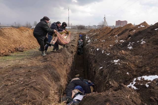 Bodies are lowered into a mass grave on the outskirts of Mariupol (AP)