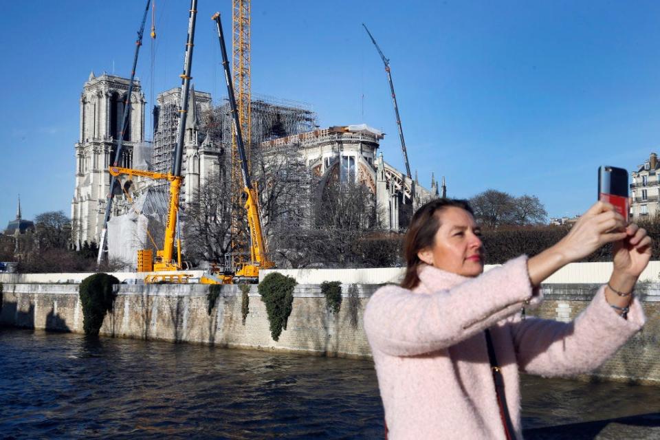 PARIS, FRANCE - DECEMBER 18: A tourist takes a selfie with Notre-Dame cathedral more than eight months after the fire that ravaged the emblematic monument on December 18, 2019 in Paris, France. A fire broke out in Notre- Dame Cathedral in the evening of Monday, April 15, and quickly spread to the building's wooden roof destroying the famous spire. The cleaning and consolidation phase of the building should continue until the end of the year. (Photo by Chesnot/Getty Images)