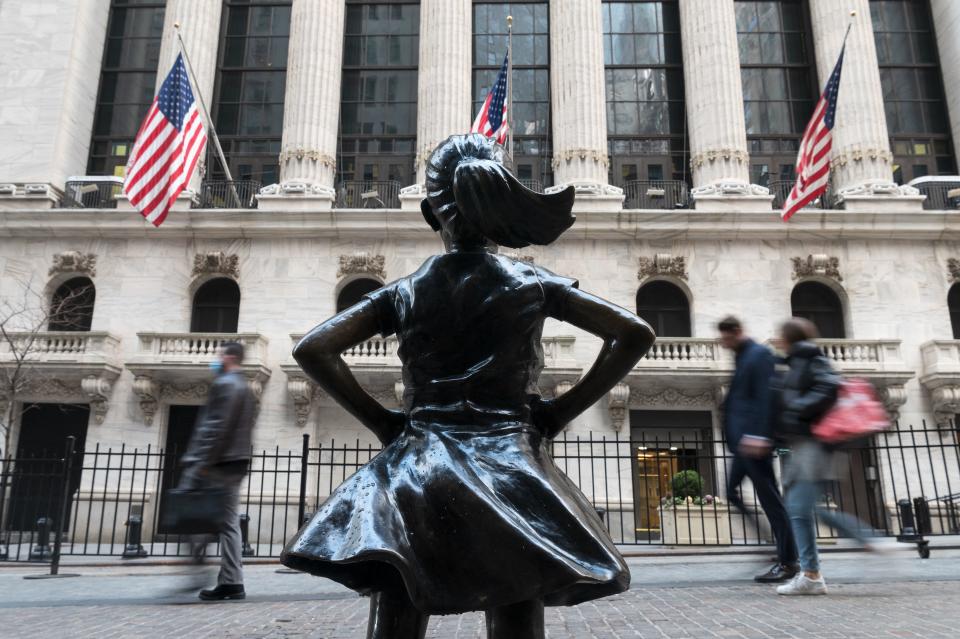 People walk past the New York Stock Exchange (NYSE) at Wall Street and the  'Fearless Girl' statue on March 23, 2021 in New York City. - Wall Street stocks were under pressure early ahead of congressional testimony from Federal Reserve Chief Jerome Powell as US Treasury bond yields continued to retreat. (Photo by Angela Weiss / AFP) (Photo by ANGELA WEISS/AFP via Getty Images)