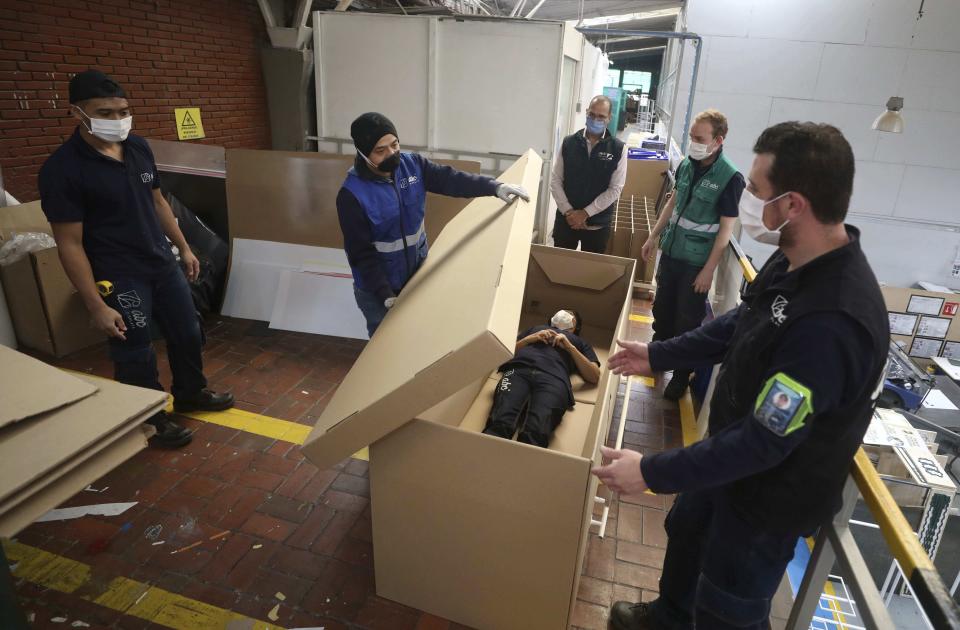 Rodolfo Gomez, to center, and his employees demonstrate how their design of a cardboard box can serve as both a hospital bed and a coffin, designed for COVID-19 patients, in Bogota, Colombia, Friday, May 8, 2020. Gomez said he plans to donate the first units to Colombia's Amazonas state, and that he will sell others to small hospitals for 87 dollars. (AP Photo/Fernando Vergara)