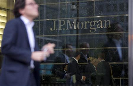 Workers are reflected in the windows of the Canary Wharf offices of JP Morgan in London in this file photo from September 19, 2013. JPMorgan Chase & Co, the largest U.S. bank, is reducing both its profit target and headcount in 2014, according to a Tuesday presentation. REUTERS/Neil Hall/Files