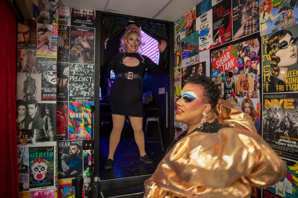 A drag queen backstage, putting on a gold dress
