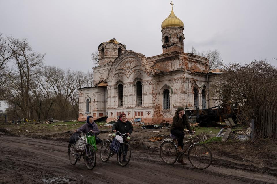 Residents walk with their bicycles in front of a damaged church, in Lukashivka, in northern Ukraine, Friday, April 22, 2022. A single metal cross remains inside the Orthodox church of shattered brick and blackened stone. Residents say Russian soldiers used the house of worship for storing ammunition, and Ukrainian forces shelled the building to make the Russians leave. (AP Photo/Petros Giannakouris) ORG XMIT: XPG101