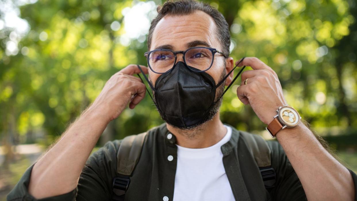 portrait of mature man walking and putting on face mask outdoors in park