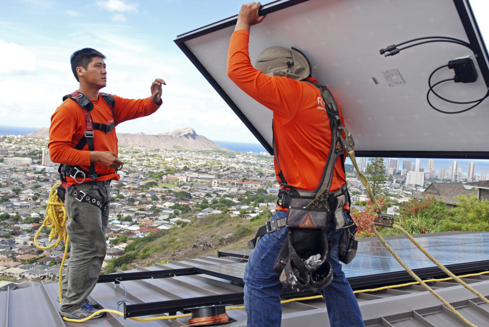 FILE - In this July 8, 2016, file photo, Dane Hew Len, left, lead installer for RevoluSun, and installer Radford Takashima place solar panels on a roof in Honolulu. If you have the cash, most experts agree buying a solar system outright is a better investment than leasing or taking out a loan. Customers should check electric bills to estimate monthly energy use when deciding what size system to buy, and calculate federal or state incentives. (AP Photo/Cathy Bussewitz, File)