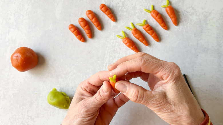 Shaping carrot stems out of green marzipan and inserting into carrot tops
