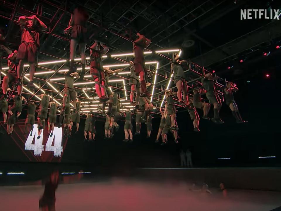 Four dozen people hanging from a structure with only their arms above a pool of water.