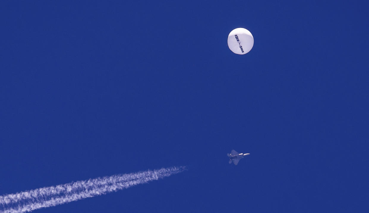 A large balloon drifts above the Atlantic Ocean, with a fighter jet and its contrail seen below it.