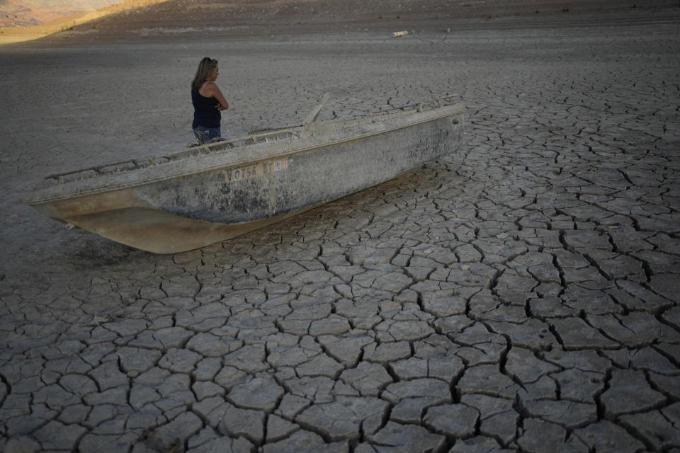 Misha McBride looks at a formally sunken boat now on cracked earth hundreds of feet from what is now the shoreline on Lake Mead at the Lake Mead National Recreation Area, Monday, May 9, 2022, near Boulder City, Nev. Las Vegas is being flooded with lore about organized crime after a second set of human remains emerged within a week from the depths of the drought-stricken Colorado River reservoir just a 30-minute drive from the notoriously mob-founded Strip. (AP Photo/John Locher)