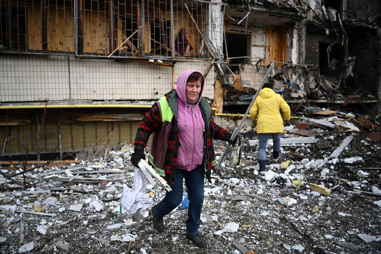 Women clear debris at a damaged residential building.