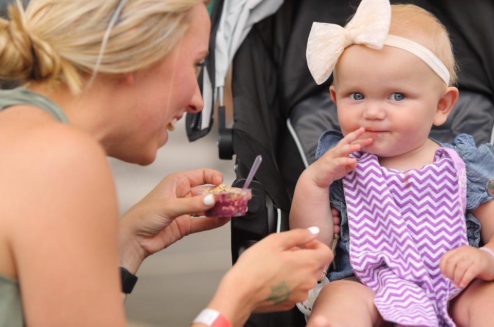 Braleigh Robertson smiles as her mom Alyssa Robertson feeds her a tasty treat from Rush Bowls at the Taste of Bloomington festival in Showers Plaza Saturday, June 22, 2019. (Rich Janzaruk / Herald-Times)