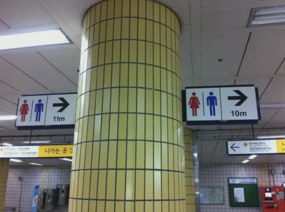 Signs in a subway station indicating restrooms, with conflicting arrow directions and distances