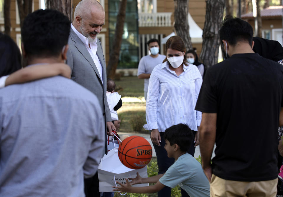 Albanian Prime Minister Edi Rama offers a gift to a boy during his visit at a resort which is accommodated Afghan refugees in Golem, 45 kilometres (30 miles) west of the capital Tirana, Friday, Aug. 27, 2021. Albania on Friday housed its first group of Afghan evacuees who made it out of their country despite days of chaos near the Kabul airport, including an attack claimed by the Islamic State group. (AP Photo/Franc Zhurda)