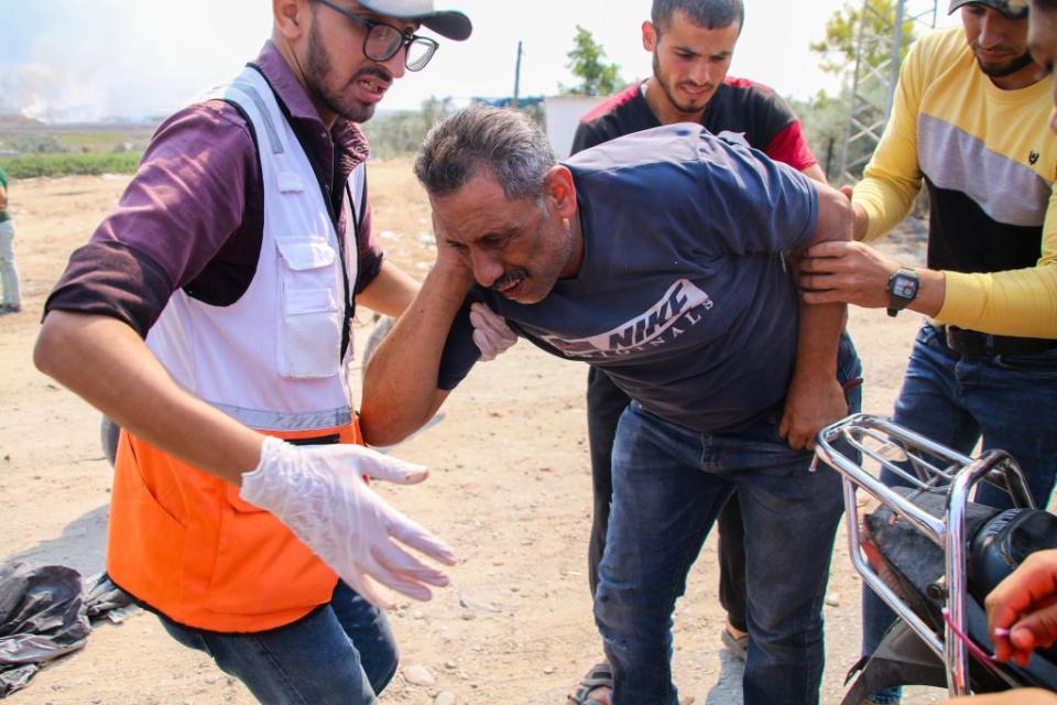A paramedic helps an injured man near the border fence between the Gaza Strip and Israel on October 7, 2023, in Gaza City, Gaza. The Palestinian militant group Hamas launched a missile attack on Israel today, with fighters simultaneously crossing the border from Gaza. Israel has declared a state of war.