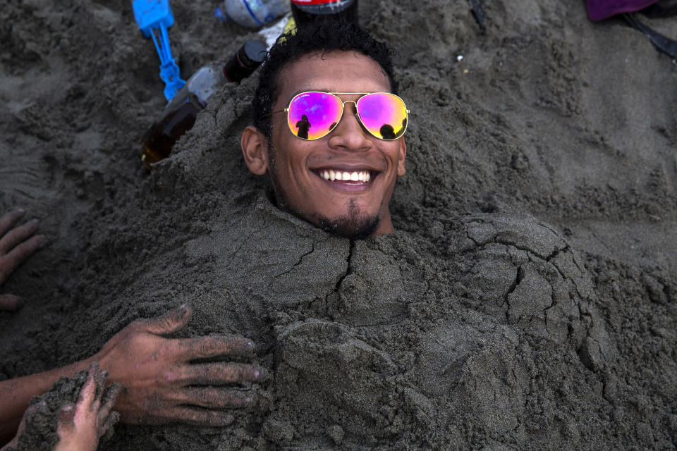 En esta imagen, tomada el 16 de febrero de 2020, un hombre sonríe mientras es enterrado por sus amigos en la arena durante una jornada de playa en Agua Dulce, Lima, Perú. (AP Foto/Rodrigo Abd)