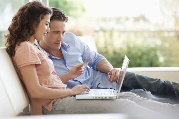 A man and woman looking at a computer screen while holding a credit card.