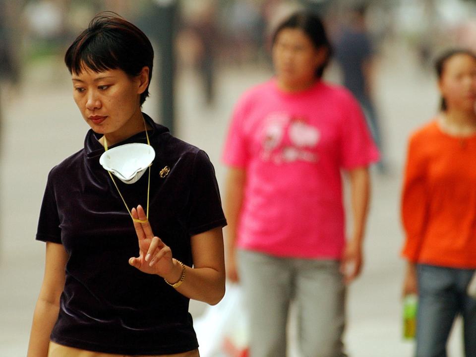 A woman plays with a protective mask at a shopping street in 2003 in Beijing.