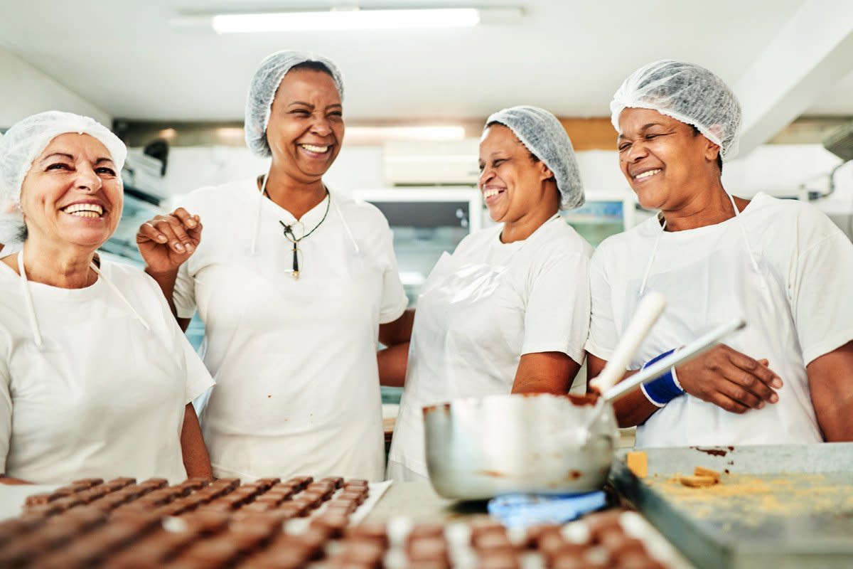 A group of women laugh as they bake desserts.