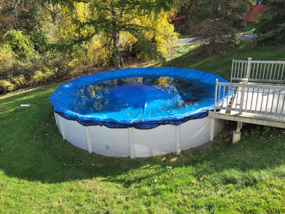 A round, above-ground pool closed for the winter with blue cover and wood deck.