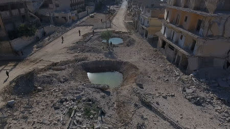 A still image taken on September 27, 2016 from a drone footage obtained by Reuters shows people standing near craters and damaged buildings in a rebel-held area of Aleppo, Syria. Handout via Reuters TV