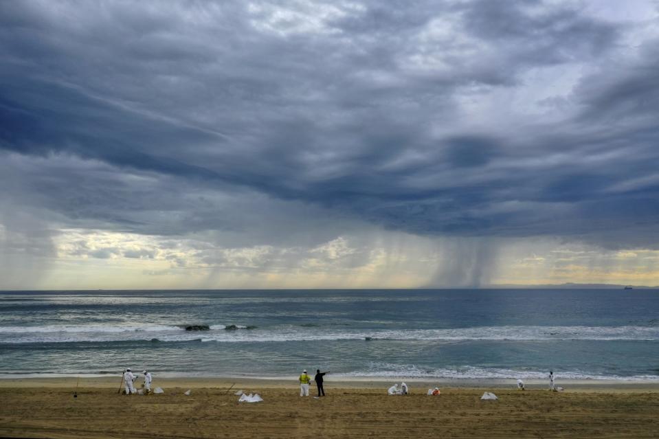 A storm rolls in as cleanup crews spread out across Huntington State Beach.