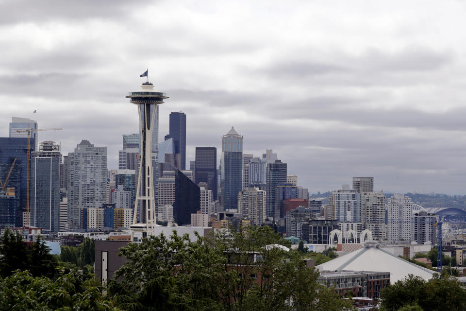 A flag with the new logo for the newly-named Seattle NHL hockey team, the Seattle Kraken, flies atop the iconic Space Needle and in view of the team's arena, lower right, Thursday, July 23, 2020, in Seattle. The hockey expansion franchise unveiled its nickname Thursday, ending 19 months of speculation about whether the team might lean traditional or go eccentric with the name for the league's 32nd team. Seattle's colors are a deep dark blue with a lighter shade of blue as a complement. (AP Photo/Elaine Thompson)