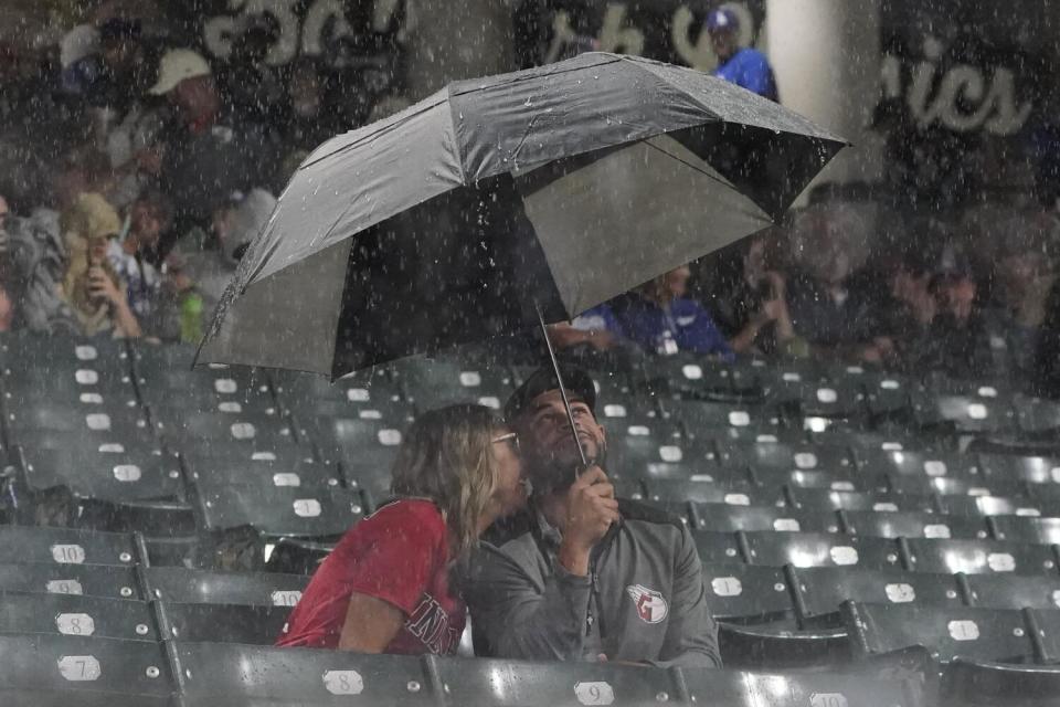 Fans sit under an umbrella during a rain delay in the third inning of a game between the Dodgers and the Cleveland Guardians.