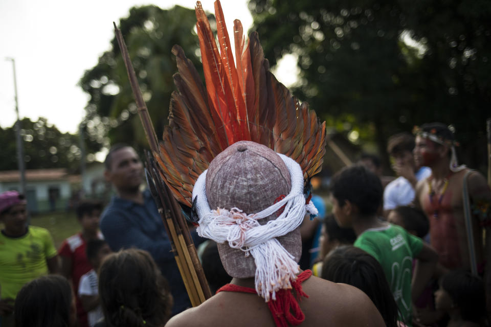 In this Sept. 3, 2019 photo, a villager wears a baseball cap to hold his feather headdress during a meeting of Tembé tribes at the Tekohaw indigenous reserve, Para state, Brazil. Classes had been canceled that day and life in the village seemed to have been put on hold so the Tembé tribes could debate the pros and cons of the project for hours, switching between Portuguese and their native Tupi-Guarani tongue. (AP Photo/Rodrigo Abd)