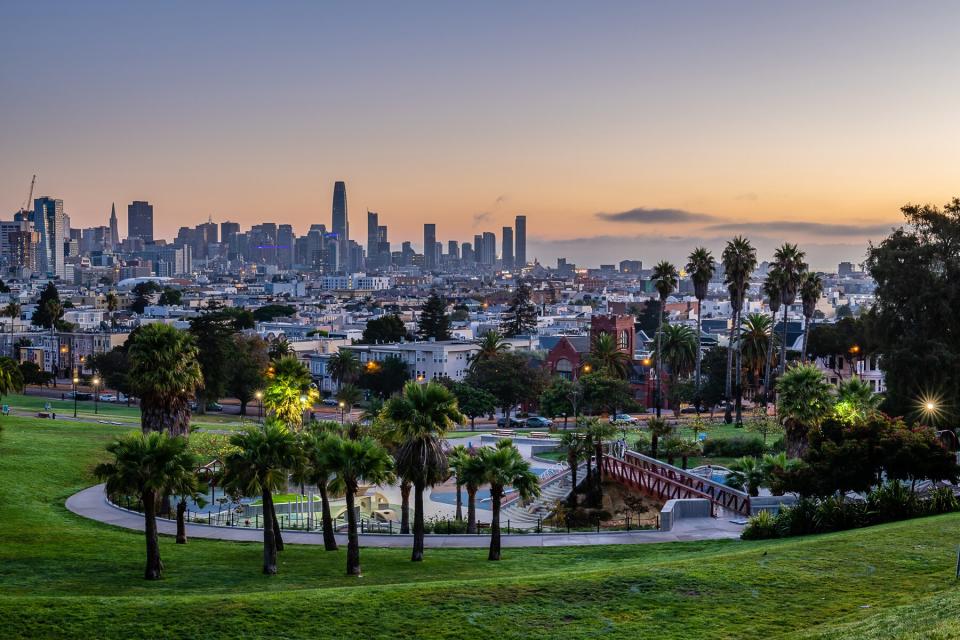 sun rises over the San Francisco skyline from Mission Dolores Park