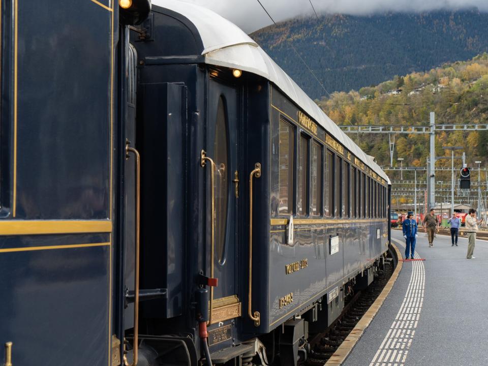 A navy blue train stopped at a platform with mountains in the background.